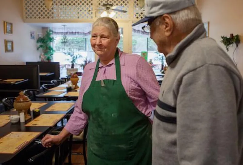 Woman in pink shirt with green apron speaking with a man in a restaurant